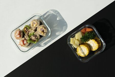 Top view of bread roll and grill vegetables in glass contain box over black and white pattern...