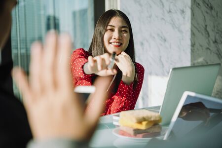 Beautiful young asian thai businesswoman in red shirt making presentation with co-worker colleague in meeting room. Beautiful boss business girl. People raise hand in meeting progress.の写真素材