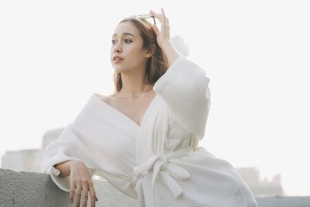 Copy space - Sexy young woman in white bathrobe at apartment balcony over city background.の写真素材