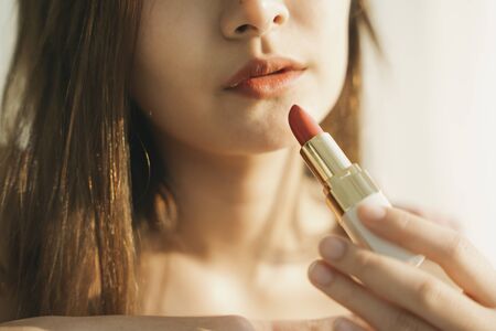 Close up of beautiful asian thai woman holding lipstick. Cosmetic concept. Warm light in the morning.の写真素材
