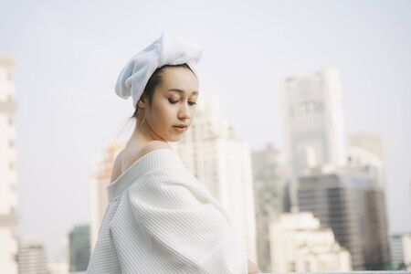 Back view - Young woman in white bathrobe with sexy posing over city background.の写真素材