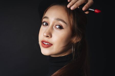 Close up portrait of pretty beautiful young woman wearing black sweater isolate over dark background. Woman using red lipstick. Cosmetic concept.の写真素材