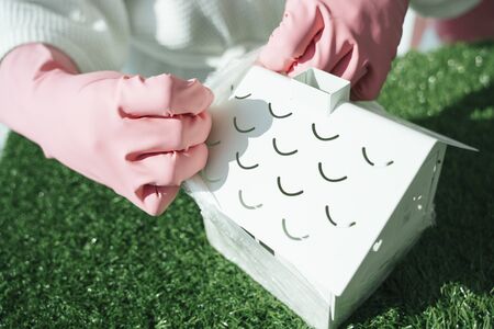 Doctor hands wearing pink gloves uncover plastic wrap from toy white house. Covid-19 concept. Doctor try to save people in the house.の写真素材