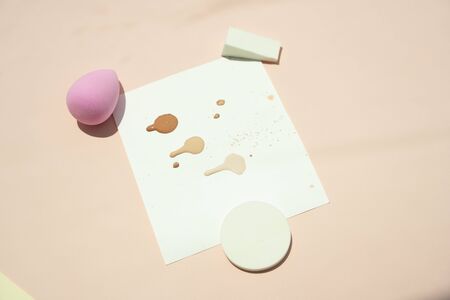 Powder puff sponge and liquid cosmetic on testing paper over beige background.