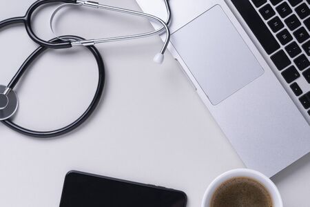 Top view - Doctor working table with stethoscope, laptop, book and eyeglasses over grey background.の写真素材