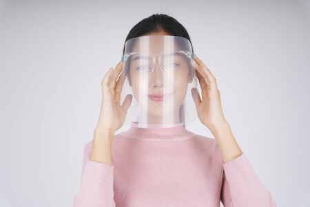 New normal life - Asian thai woman wearing face shield and mask using smartphone at home.の写真素材