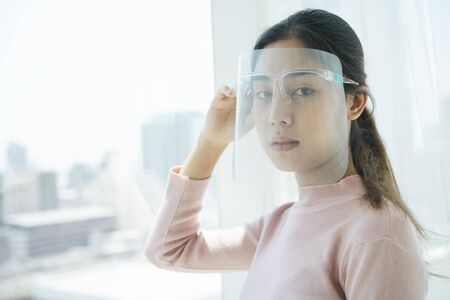 New normal life - Asian thai woman wearing face shield and mask using smartphone at home.