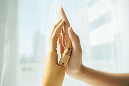 Hand of wooden cyborg robot and human touching each other.