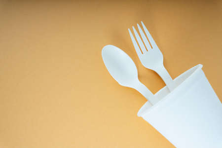 Plastic spoon and fork in a cup over orange background. Disposable utensil.の写真素材