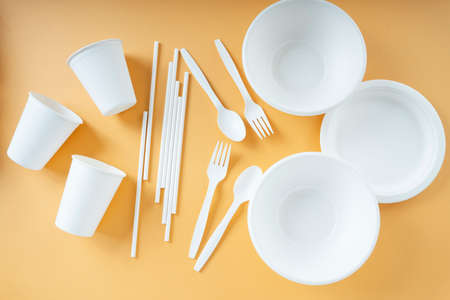 Disposable plastic cup, fork, spoon, bowl, pan,and straw over orange background.の写真素材