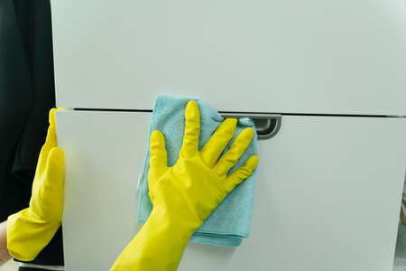 Hand wearing yellow gloves cleaning furniture with rag. Covid-19 Coronavirus prevention.の写真素材