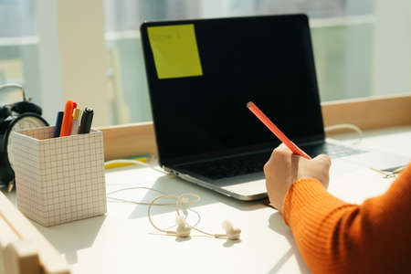 Student taking note with pencil on a book. Study and learn from home at working desk laptop.