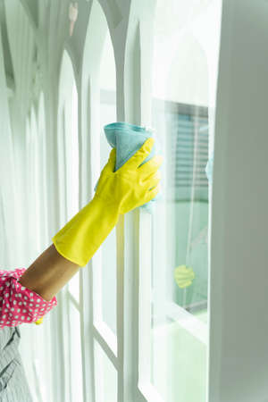 Maid hand wearing yellow gloves cleaning washing mirror with pink rag cloth. Covid-19 Coronavirus prevention.の写真素材