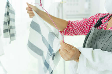 Maid woman hanging cloth after laundry on a rack.