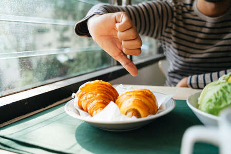Cropped image of a man's hand, he give a croissant thumb down because it's unhealthy.