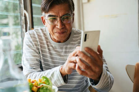 Old man with gray hair wearing eyeglasses sitting on sofa and enjoy talking to his friend.