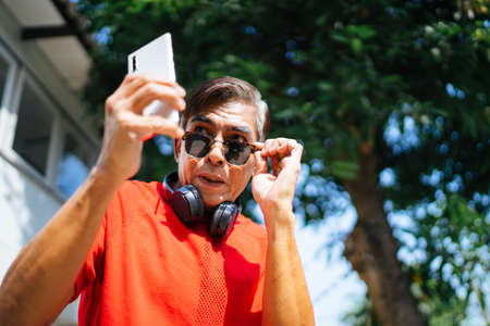 Old man in red t-shirt enjoy the music from mobile application in sunny day at his home.の写真素材