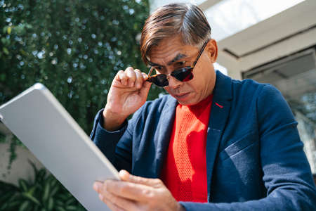 Reflection in a mirror of old man while he use tablet for social media.