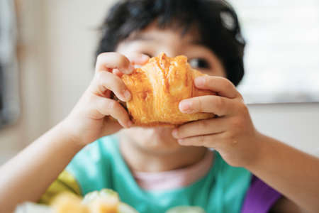 Cropped image of sausage croissant while little boy bite and eat it deliciously for his breakfast in the kitchen.の写真素材