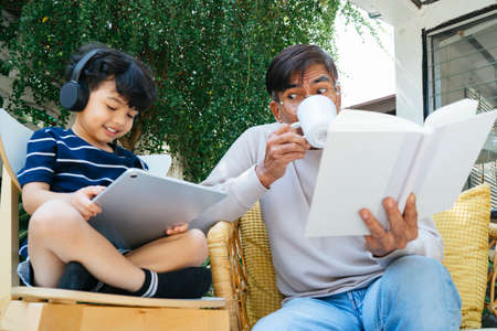 Little boy wearing the headphone to listen the music and read the e-book from tablet while the old...