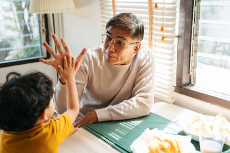Little boy hit the hand with his grandpa during their breakfast.の写真素材