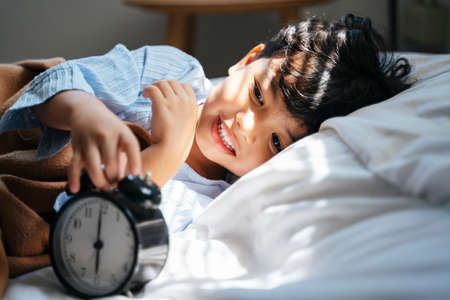 Little boy lie down in the cozy bed, he just wake up from the daytime sleep by the alarm clock.