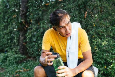 Old man in yellow t-shirt get some rest from jogging, he drink the water from green sport bottle and...