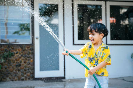 Little boy splash the water with water gun and rubber tube at his house in Songkran day, the yearly traditional day of Thailand.の写真素材