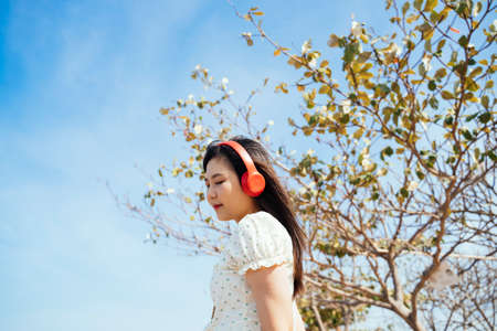 Long hair girl wearing red headphone to listening the song under the tree in blue sky.
