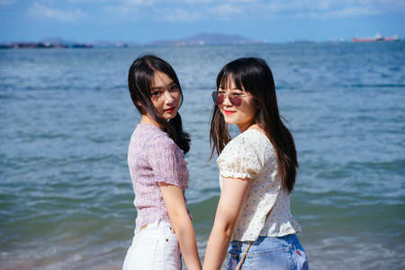 Two girls hold each other hands, walking on the beach at the sea in windy day.の写真素材