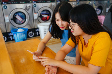 Two girls sitting back to back on the mat on the field, play the bubble andpurple flowers.