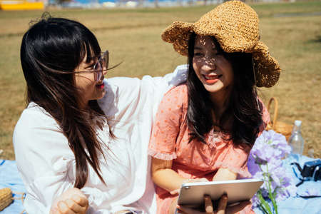 A girl in brown hat take a photo of her friend while theyr sitting on the beach next to the sea in...