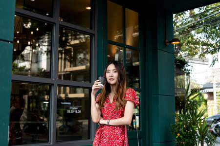 Young asian woman on red dress holding a cup of coffee at cafe outdoors.