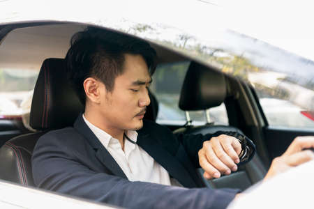 Dangerous situation - Asian thai businessman on formal suit using mobile phone while driving a car on the road.の写真素材