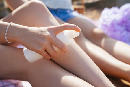 Cropped image of woman's hand spray the sunscreen on the legs while travel at the sea.の写真素材