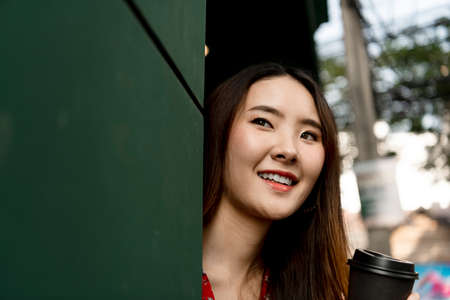 Close up Young asian woman on red dress enjoy drinking coffee on the street.