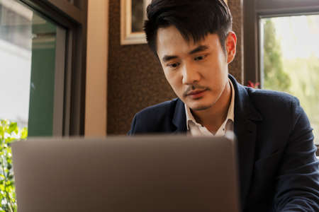 Serious asian thai businessman on formal suit working on laptop at office space.
