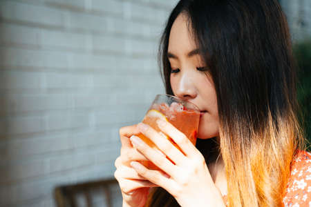 Close up Young asian thai woman on red dress drinking or sipping ice cold juice, holding it with two...