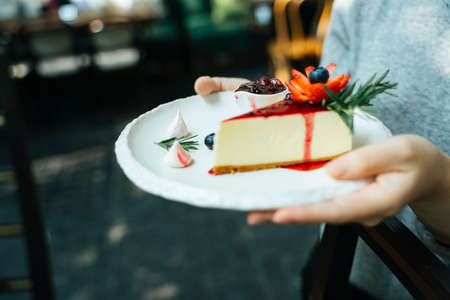 Hand of waitress holding a plate with slice of cheesecake and blueberry on top of it.の写真素材