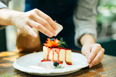 Woman pastry chef pouring strawberry jam into cheesecake. Dessert happiness.の写真素材