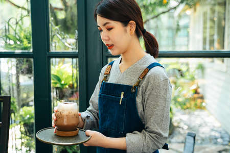 Beautiful asian thai waitress serving ice cold coffee to customer at cafe.