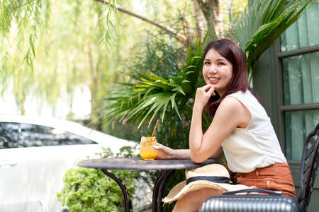 Beautiful cheerful asian thai woman sitting on a chair outdoor with tropical passion fruit juice.の写真素材