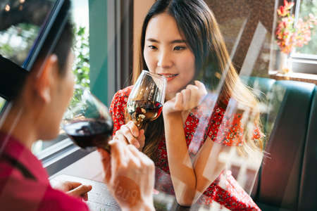 Beautiful asian woman drinking red wine with boyfriend at restaurant on Valentine day. Toasting with the man.の写真素材