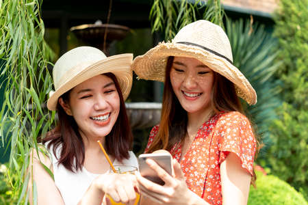 Two young beautiful asian women wearing hat on vacation. Travel together at resort.の写真素材