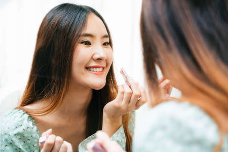 Close up face of asian thai woman long hair applying lipstick in front of the mirror.の写真素材