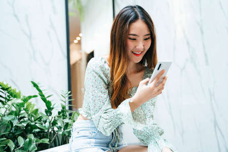 Beautiful long hair asian thai woman holding using smartphone, talking and texting with friends,...