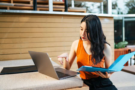 Portrait of Sexy asian beautiful woman wearing orange shirt holding laptop, talking on the phone at...