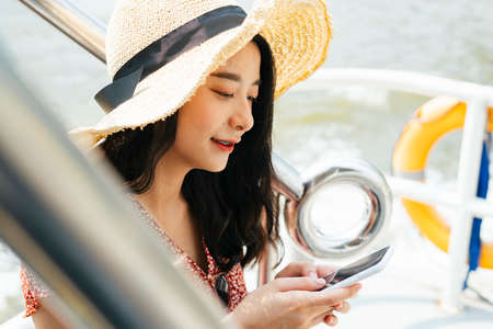 Young beautiful Thai asian traveler woman wearing red dress and hat standing on a pier at Chao Praya...