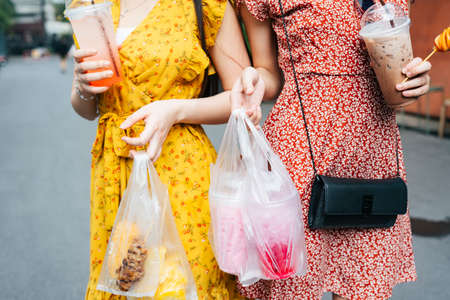 Beautiful asian woman wearing red dress eating street food with friend on yellow dress together on the street - Street food.の写真素材