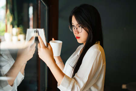 Cheerful smiling asian woman wearing eyeglasses holding a cup of coffee in the morning.